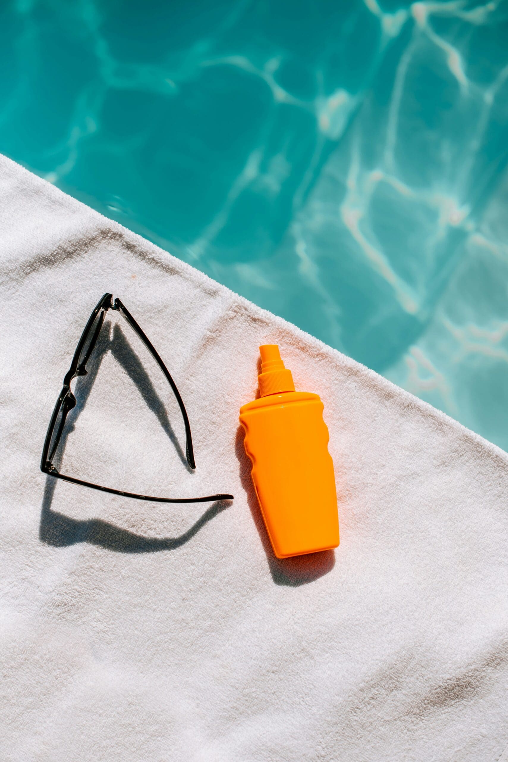 Flat lay of sunscreen and sunglasses by a poolside, promoting UV protection and summer skincare essentials